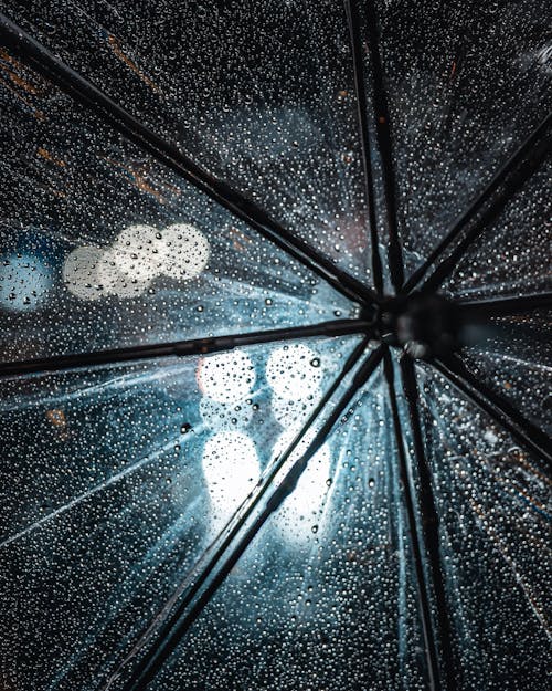 Closeup of transparent umbrella with drops from rain and reflected night lights of city