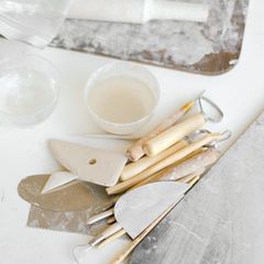 Pale clay and wooden modelling tools on a white table