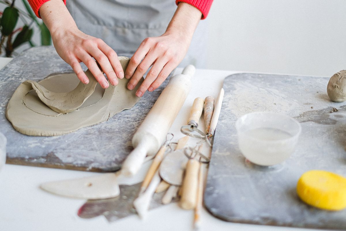 A maker shaping a slab of clay on a stone work surface. Photo by Anna Shvets on Pexels.