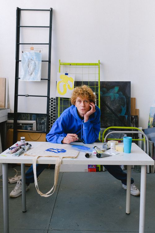 Free Full body of calm male designer looking at camera and painting while standing at table with spread legs in studio Stock Photo