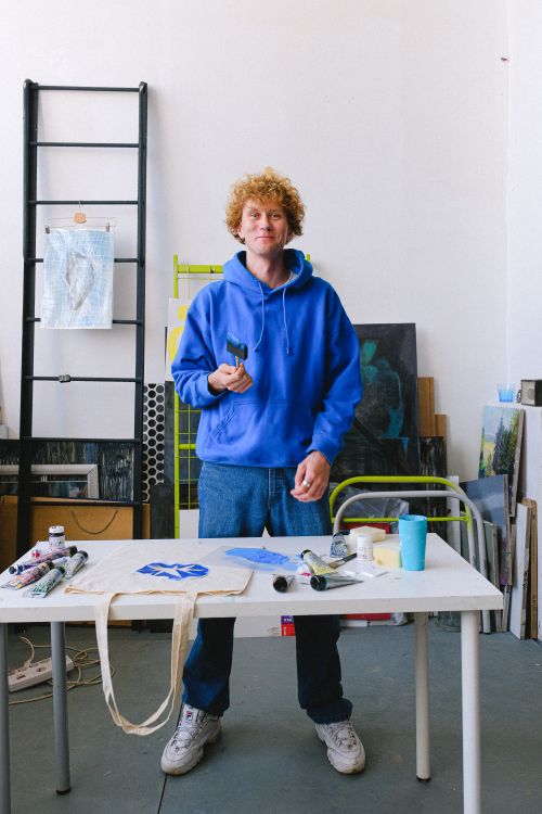 Free Full body of positive male master standing at table with equipment and printed bag in professional studio with ladder during work Stock Photo