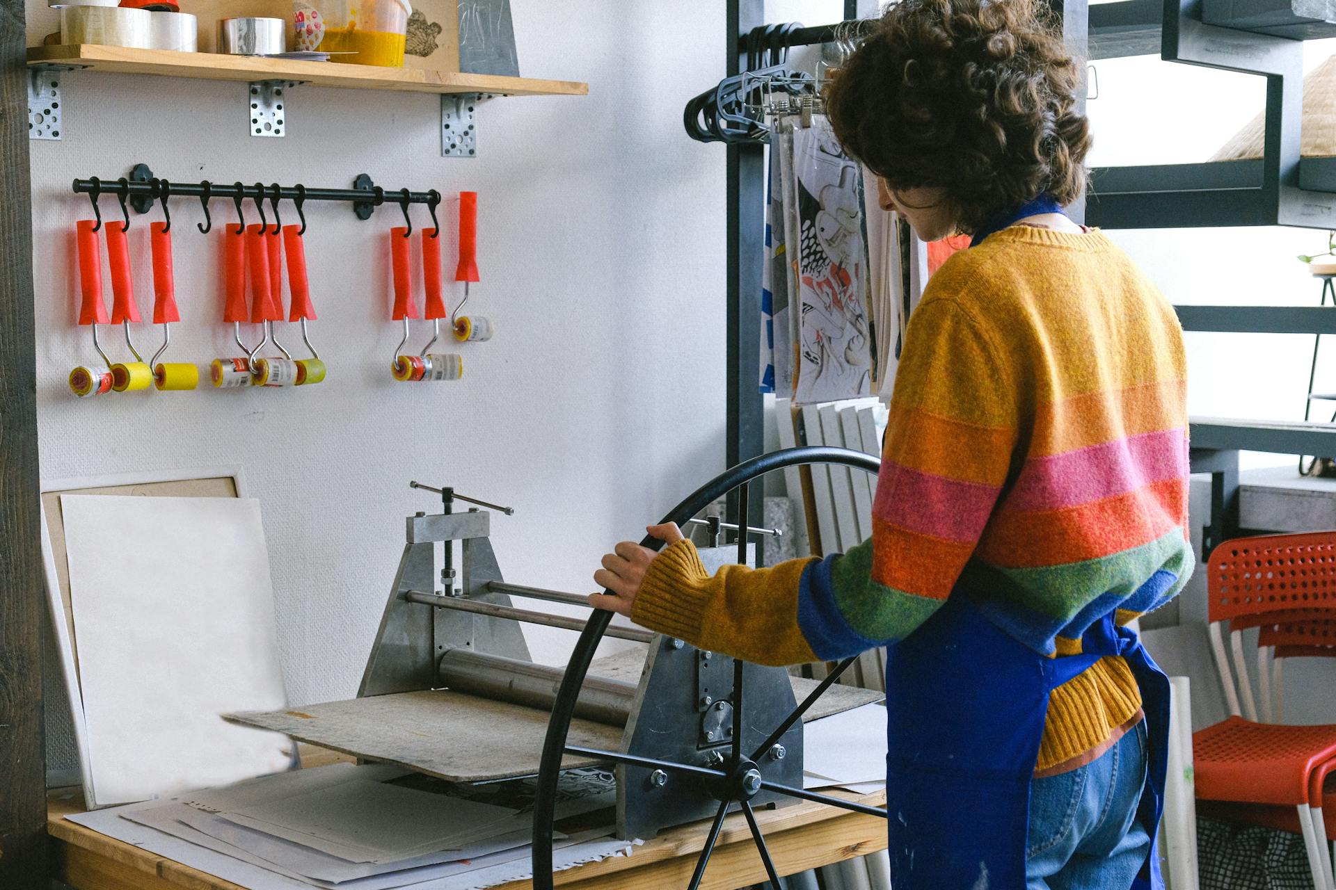 Side view of anonymous female master working at workbench with printing press with wheel in modern art studio with rollers