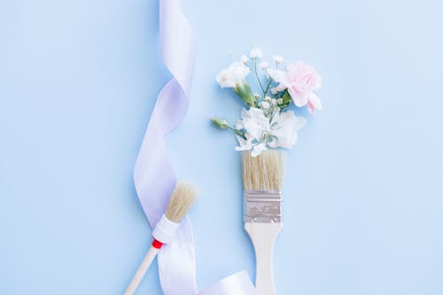 Paint Brushes, Artificial Flowers and a Ribbon on Light Blue Surface