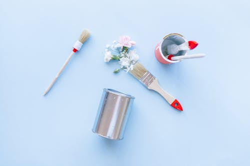 Paint Brushes, Cans and Artificial Flowers on Light Blue Background