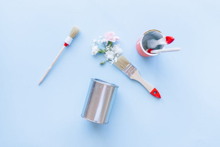 Paint Brushes, Cans And Artificial Flowers On Light Blue Background