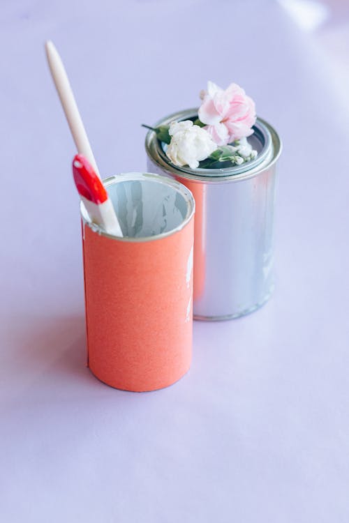 Paint Cans, Artificial Flowers and Paint Brushes on Lilac Surface