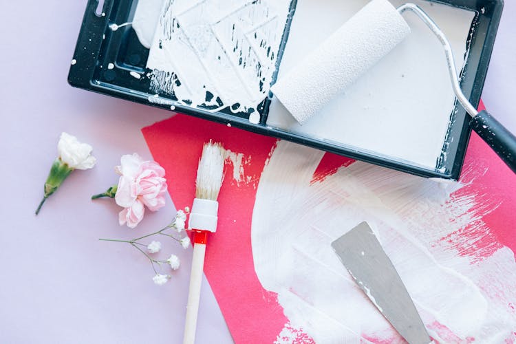 Pink Flowers Next To A Black Tray With Paint Roller