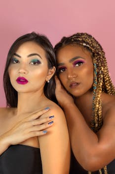 Two women showcasing vibrant makeup and natural hairstyles against a light pink background.