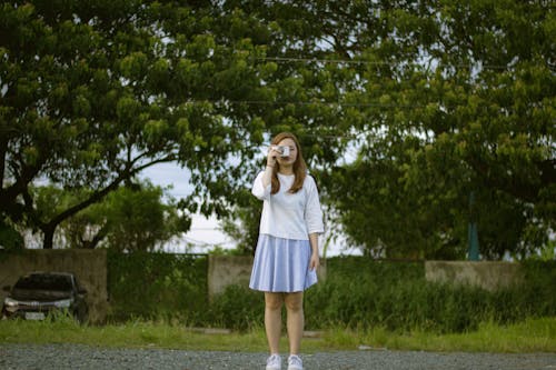 A Woman Wearing a Skirt Taking a Picture Using Her Camera