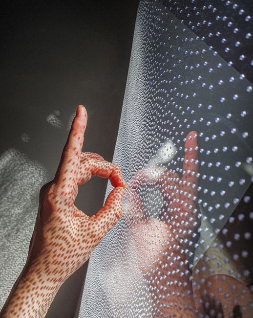 A hand making a gesture with intricate patterns reflected in light.