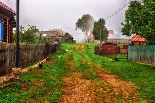 Free Idyllic rural scenery with a dirt road, fog, and rustic houses on a misty morning. Stock Photo
