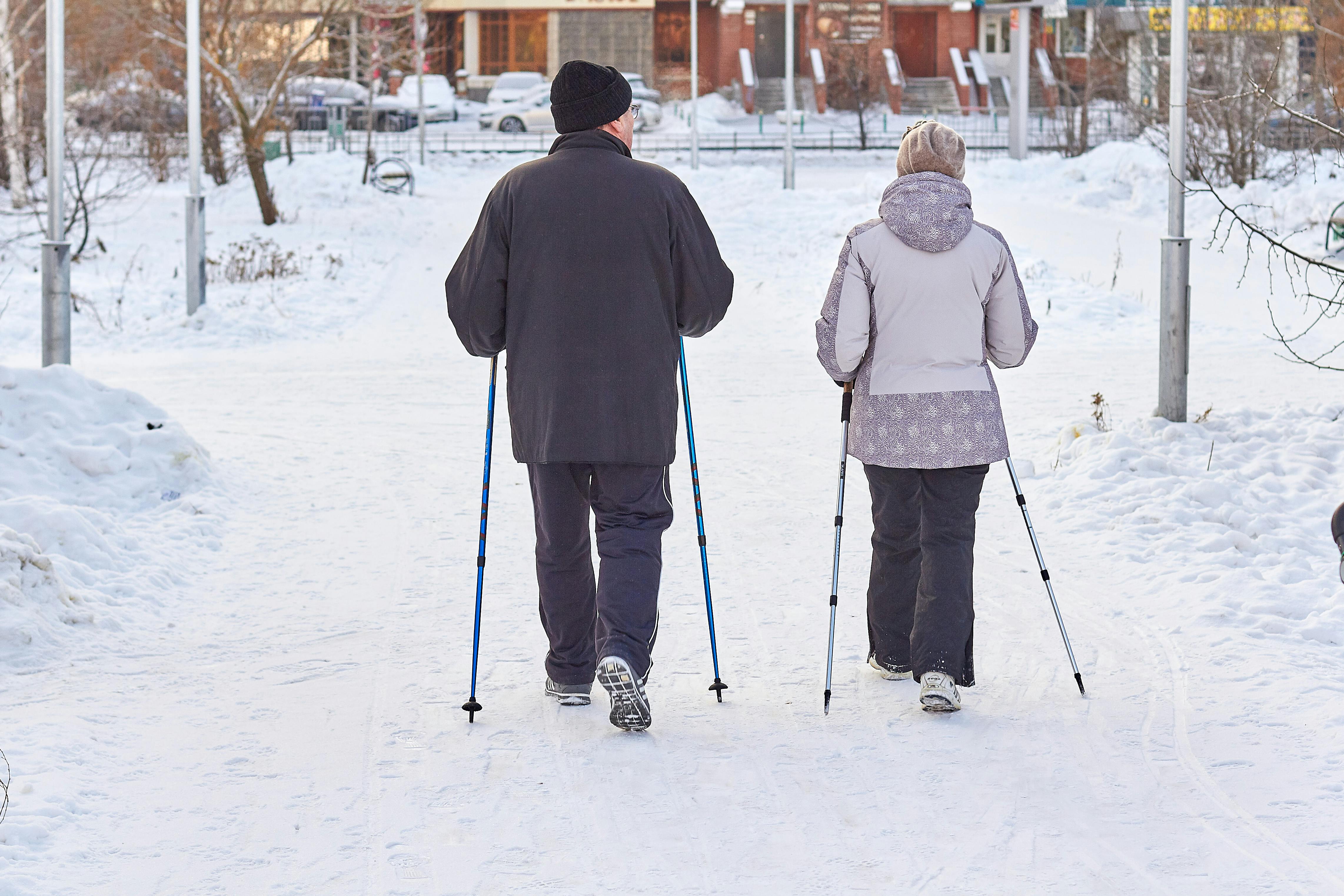 Prescription Goggle Inserts - Elderly couple enjoying a winter walk with ski poles in a snowy park setting.