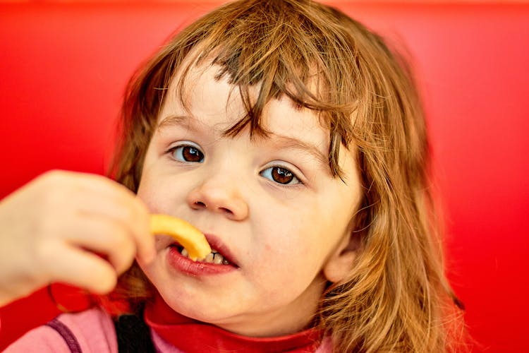 Close-Up Shot Of A Child Eating French Fries