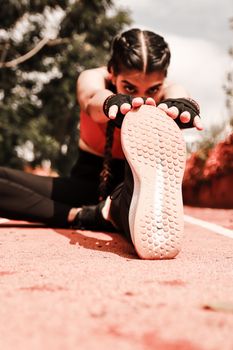 Ground level of young athletic female stretching on racetrack in sportswear in summer sunny day