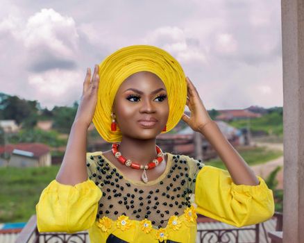 Portrait of a woman in vibrant yellow traditional attire with headscarf in Ife, Nigeria.