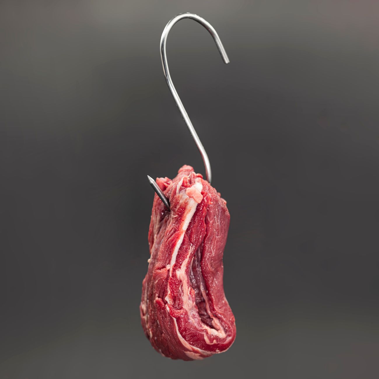 Detailed shot of raw beef suspended on a metal hook with a neutral background.
