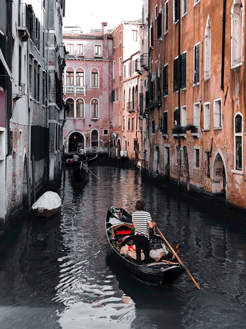 People Riding on Boat on River Between Concrete Buildings