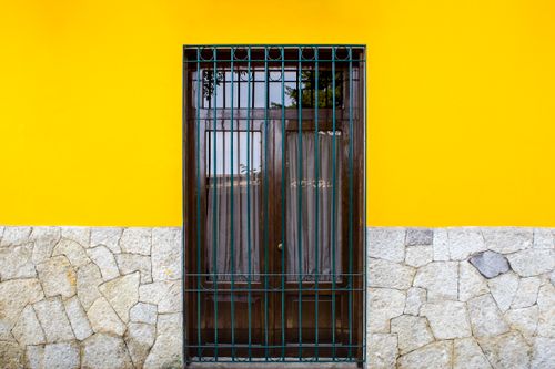 Free Exterior of wall with stony foundation and yellow wall with wooden door with metal gate in street in daytime outside Stock Photo