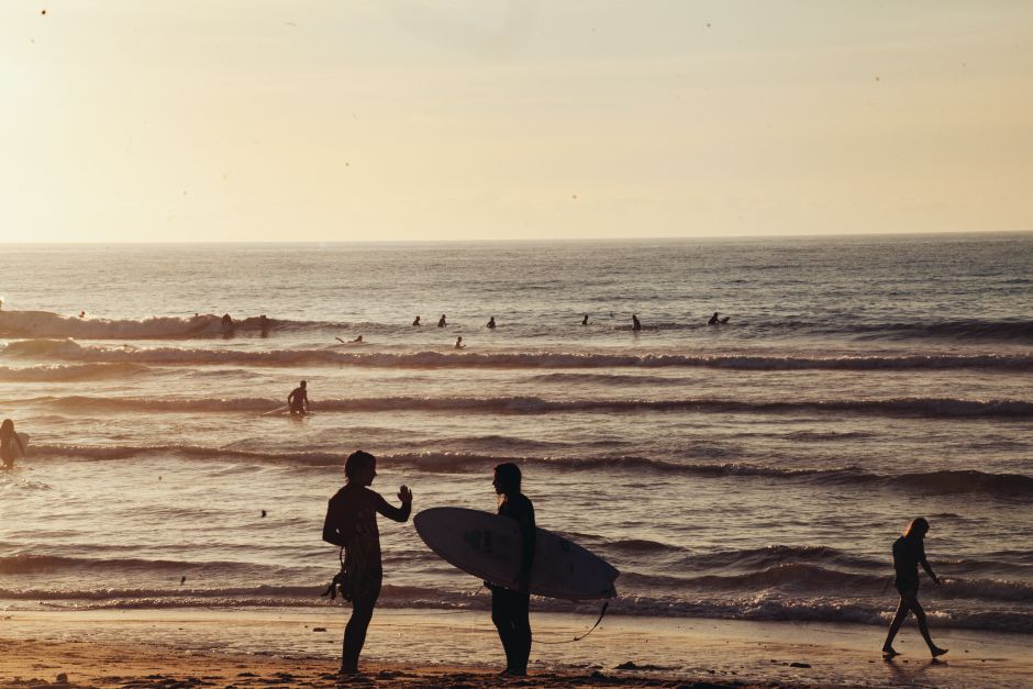 Silhouettes of surfers on a sandy beach enjoying a tranquil sunset by the ocean.
