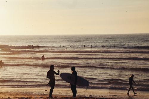 Free Silhouettes of surfers on a sandy beach enjoying a tranquil sunset by the ocean. Stock Photo