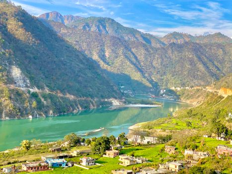 Picturesque view of a serene village nestled by a river in a mountain valley, Uttarakhand