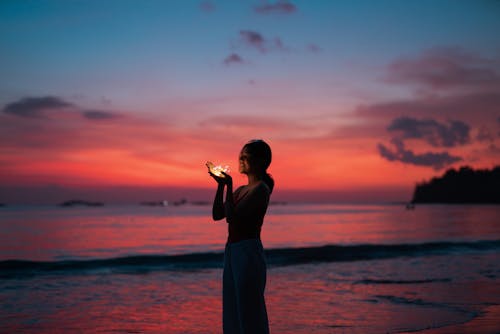 Free Woman holding lights on seashore at sunset Stock Photo