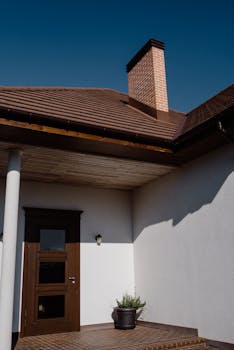 Modern house entrance featuring a wooden door and brick chimney under clear skies.