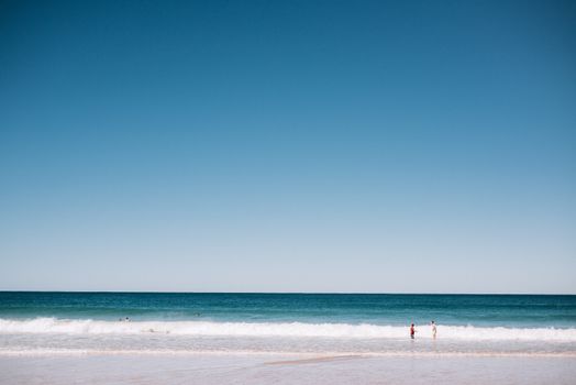 Picturesque scenery of waving endless ocean near wet sandy coast under clear blue sky