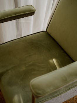 一把时尚的绿色扶手椅靠在窗边，静静沐浴着室内柔和的光线，尽显其精致设计