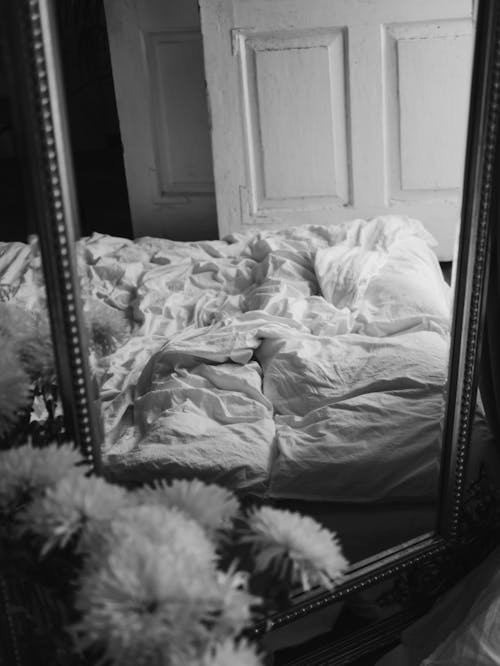 A Grayscale of a Mirror with a Reflection of a Bed