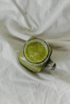 Top view of a nutritious green smoothie in a glass jar on a soft fabric background.