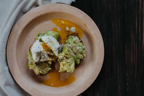 Free Mouthwatering avocado toast topped with a perfectly poached egg on a ceramic plate. Stock Photo