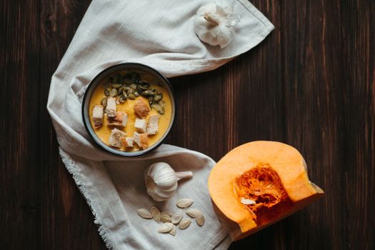 Top-down view of a delicious pumpkin soup with croutons, pumpkin seeds, garlic, and a sliced pumpkin.