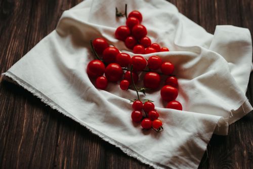 Free A close-up of vibrant cherry tomatoes on a white fabric, resting on a wooden surface. Stock Photo