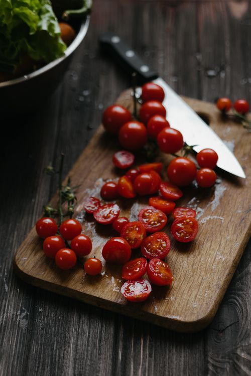 Free Sliced cherry tomatoes on a wooden chopping board with a knife, ready for a healthy salad. Stock Photo