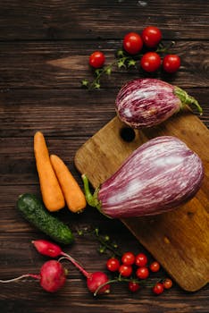 Top view of assorted fresh vegetables including carrots, eggplants, and cherry tomatoes on a wooden board.