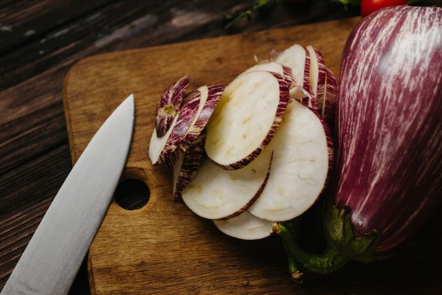Striped graffiti eggplant sliced into thin rounds on a wooden board with a knife
