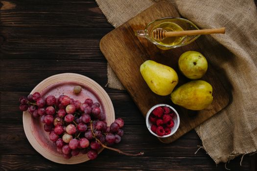A flat lay of grapes, pears, raspberries, and honey on a wooden board, enhancing healthy eating vibes.