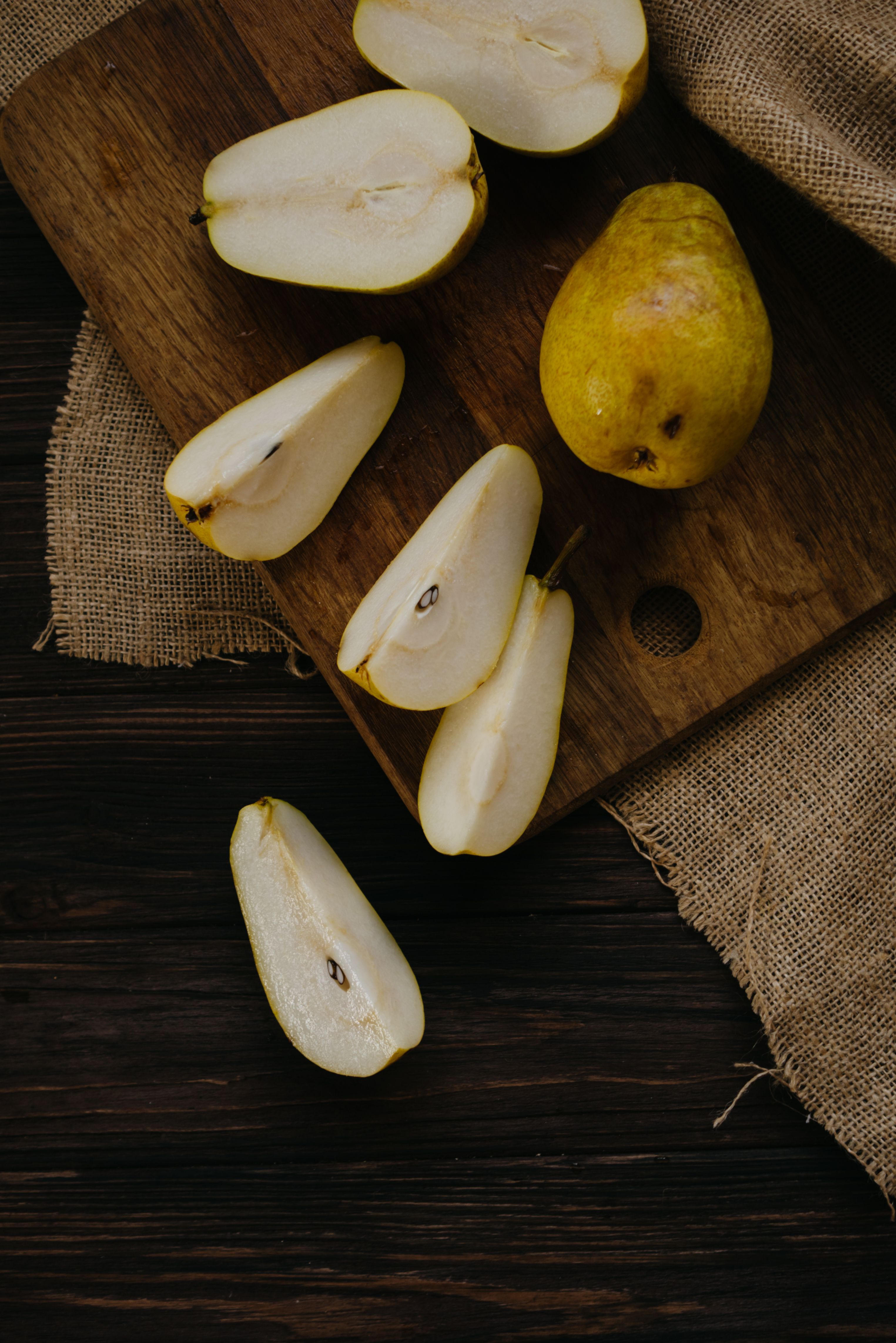 Two pale green, ridged mirliton squash on a cutting board, one halved to show the pale flesh and single flat seed inside