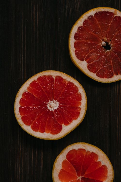 Free Juicy slices of grapefruit on a dark wooden background, showcasing fresh and healthy food. Stock Photo