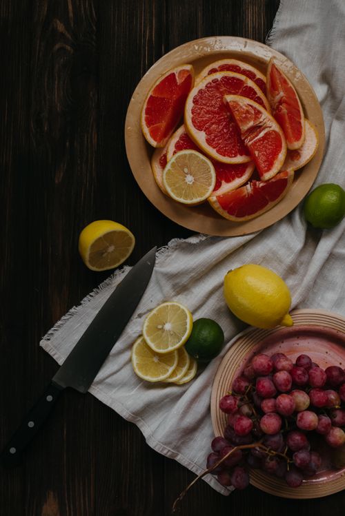 Free Freshly sliced citrus fruits with red grapes on a rustic wooden table with a knife. Stock Photo