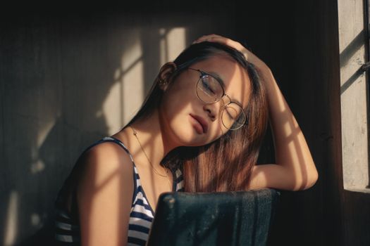 Gentle ethnic girl touching hair sitting on chair in sunshine