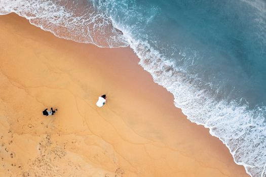 Drone view of sea waves and people relaxing on sand beach at daytime