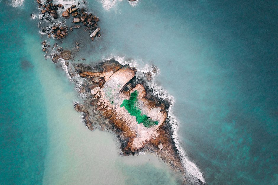 From above picturesque scenery of calm sea surface and small stony island with pond