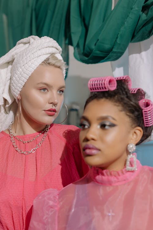 One Woman Wearing Hair Curlers and the Other Her Hair Up in a Towel 