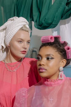 Two women posing with glamorous hairdos and makeup, one in curlers, the other with a towel wrap.
