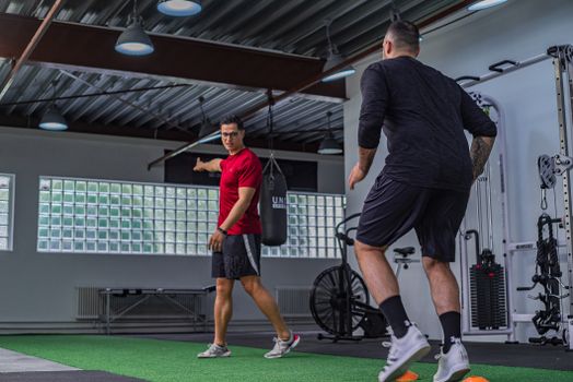 Full body of muscular sportsman in activewear doing exercises with instructor in modern gym