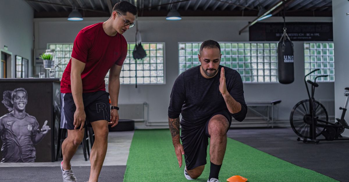 Full body of focused man in sportswear doing stretching exercises with coach in contemporary fitness center