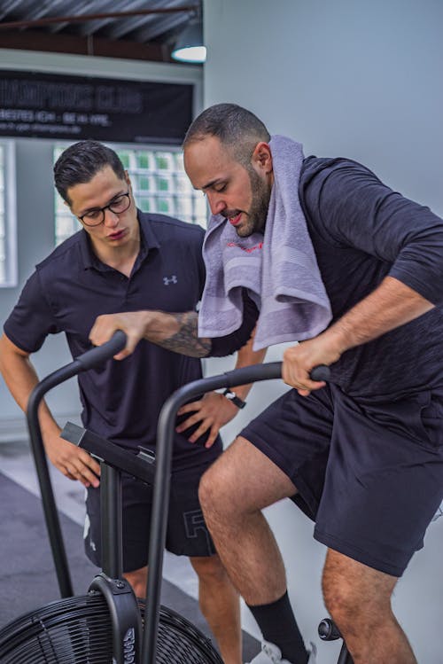 Side view of focused bearded sportsman with towel on neck doing exercise on cycling machine in gym