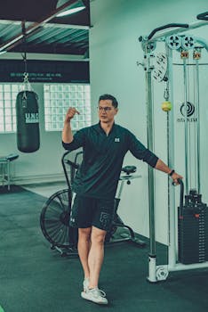 Full length of young man in sportswear standing near dumbbells and looking away while resting